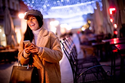 Beautiful young woman using her mobile phone in the street at Christmas time