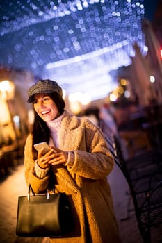 Beautiful young woman using her mobile phone in the street at Christmas time