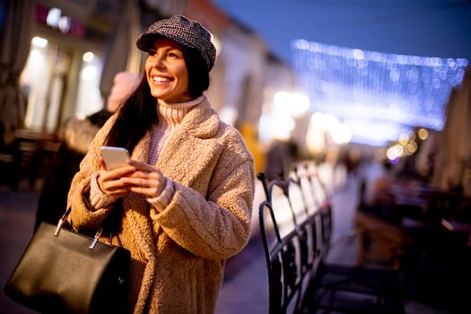 Beautiful young woman using her mobile phone in the street at Christmas time