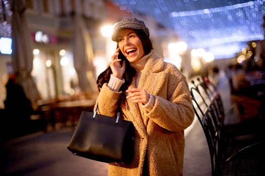 Beautiful young woman using her mobile phone in the street at Christmas time