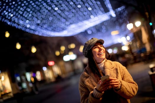 Beautiful young woman using her mobile phone in the street at Christmas time