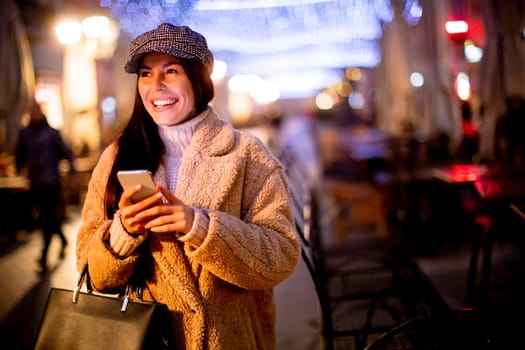Beautiful young woman using her mobile phone in the street at Christmas time