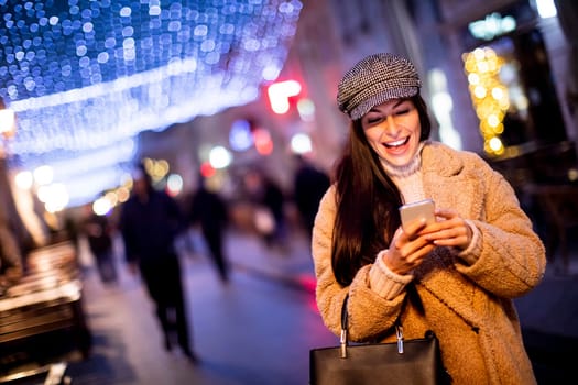 Beautiful young woman using her mobile phone in the street at Christmas time