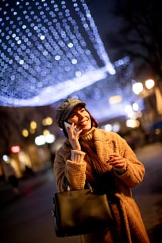 Beautiful young woman using her mobile phone in the street at Christmas time