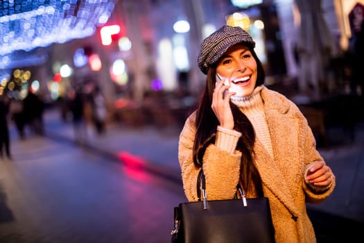 Beautiful young woman using her mobile phone in the street at Christmas time