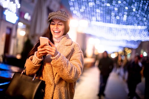 Beautiful young woman using her mobile phone in the street at Christmas time