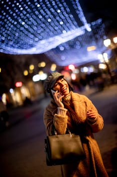 Beautiful young woman using her mobile phone in the street at Christmas time