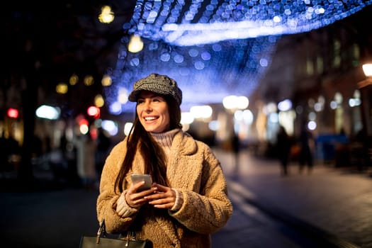 Beautiful young woman using her mobile phone in the street at Christmas time