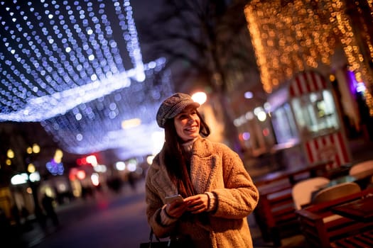 Beautiful young woman using her mobile phone in the street at Christmas time