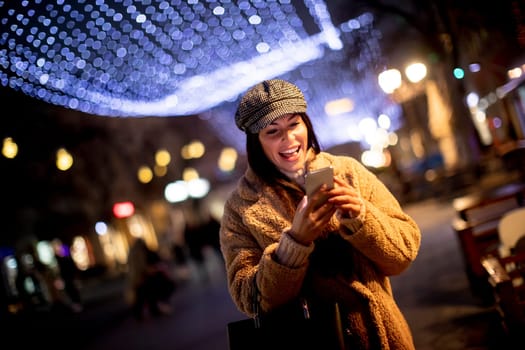 Beautiful young woman using her mobile phone in the street at Christmas time