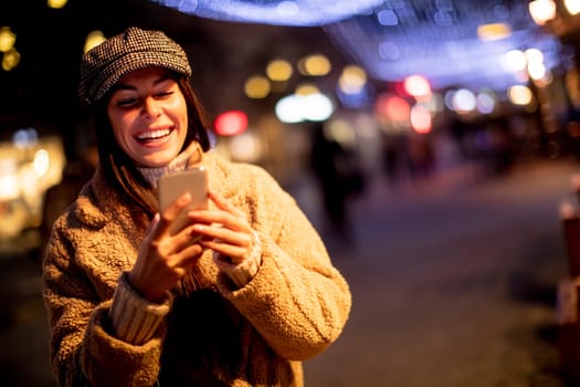 Beautiful young woman using her mobile phone in the street at Christmas time