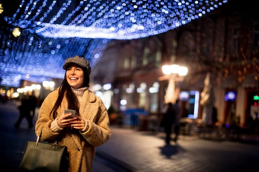 Beautiful young woman using her mobile phone in the street at Christmas time