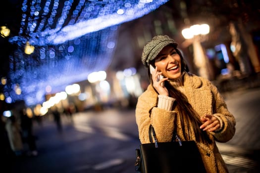 Beautiful young woman using her mobile phone in the street at Christmas time