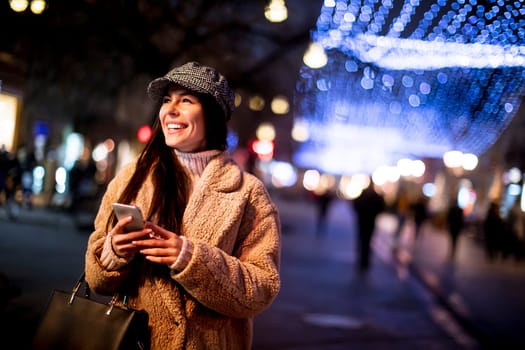 Beautiful young woman using her mobile phone in the street at Christmas time