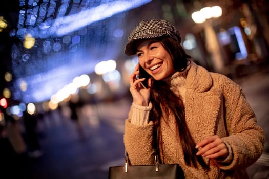Beautiful young woman using her mobile phone in the street at Christmas time
