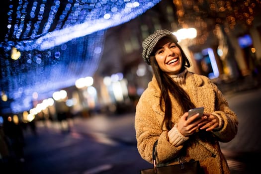 Beautiful young woman using her mobile phone in the street at Christmas time