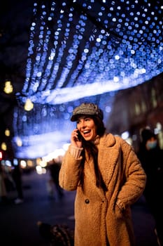 Beautiful young woman using her mobile phone in the street at Christmas time