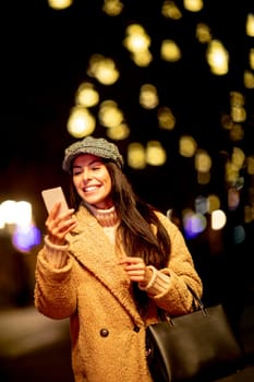 Beautiful young woman using her mobile phone in the street at Christmas time