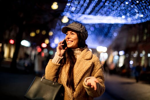 Beautiful young woman using her mobile phone in the street at Christmas time