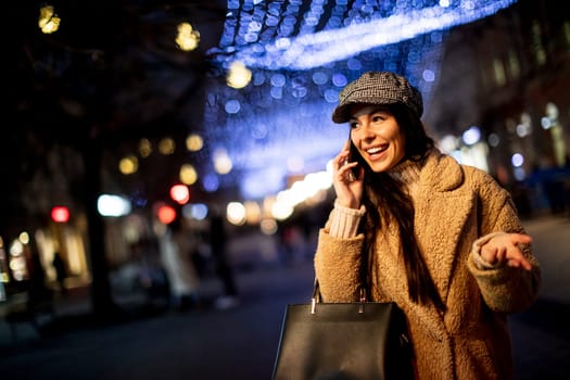 Beautiful young woman using her mobile phone in the street at Christmas time