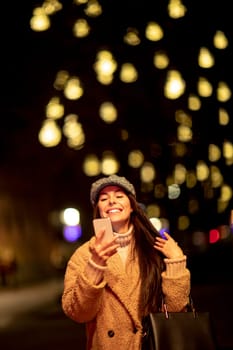 Beautiful young woman using her mobile phone in the street at Christmas time