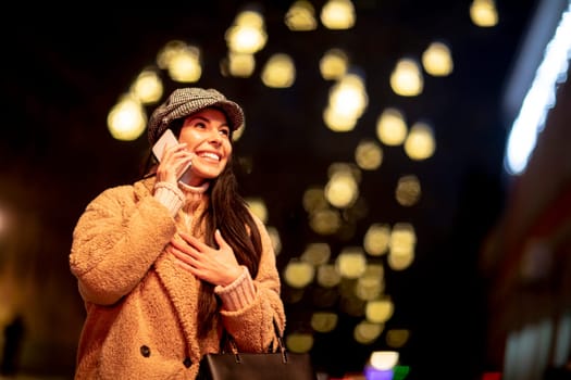 Beautiful young woman using her mobile phone in the street at Christmas time