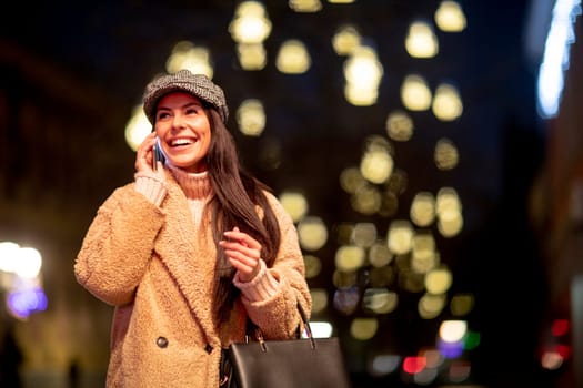 Beautiful young woman using her mobile phone in the street at Christmas time