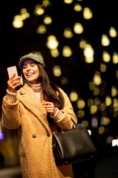 Beautiful young woman using her mobile phone in the street at Christmas time