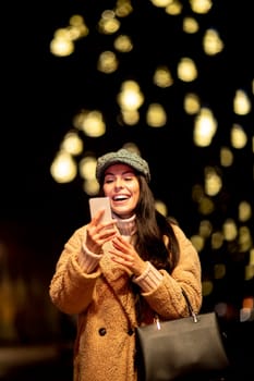 Beautiful young woman using her mobile phone in the street at Christmas time