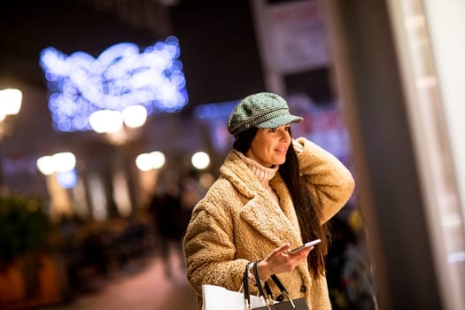 Pretty young woman with mobile phone by the shop window at Christmas time