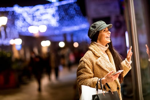 Pretty young woman with mobile phone by the shop window at Christmas time