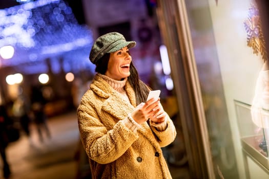 Pretty young woman with mobile phone by the shop window at Christmas time
