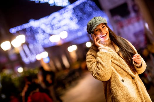 Beautiful young woman using her mobile phone in the street at Christmas time