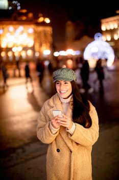Beautiful young woman using her mobile phone in the street at Christmas time