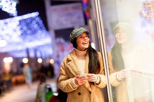 Pretty young woman with mobile phone by the shop window at Christmas time