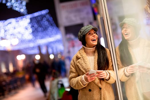 Pretty young woman with mobile phone by the shop window at Christmas time