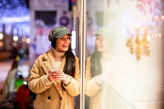 Pretty young woman with mobile phone by the shop window at Christmas time