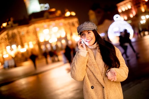 Beautiful young woman using her mobile phone in the street at Christmas time