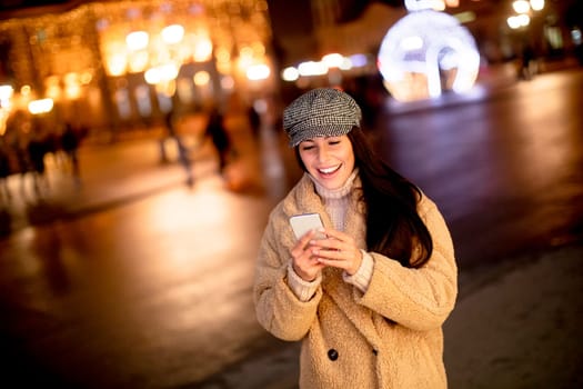 Beautiful young woman using her mobile phone in the street at Christmas time