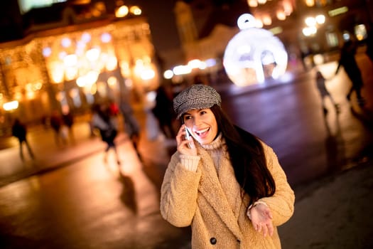 Beautiful young woman using her mobile phone in the street at Christmas time