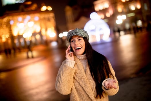 Beautiful young woman using her mobile phone in the street at Christmas time