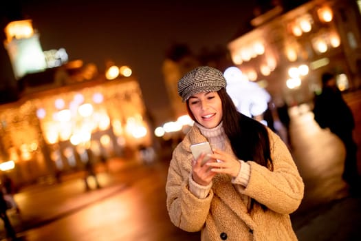 Beautiful young woman using her mobile phone in the street at Christmas time