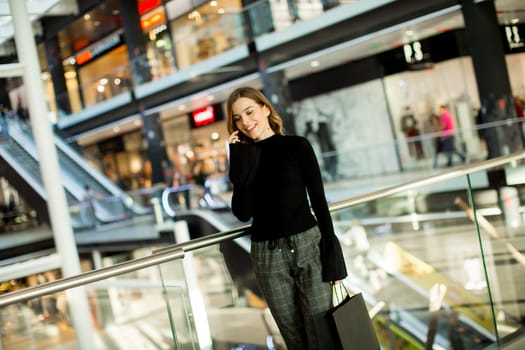 Trendy young woman shopping in mall and using mobile phone