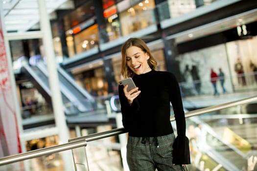 Portrait of lovely young woman looking on mobile phone in shopping center