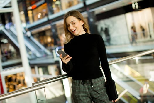 Portrait of lovely young woman looking on mobile phone in shopping center