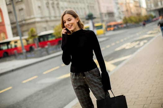 Smiling brunette woman using mobile while standing on street and  waiting for a bus or taxi