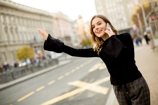 Young woman waiting for taxi or bus on the street in the city