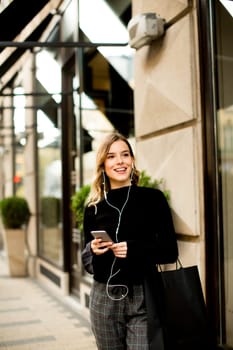 Young woman on the street with mobile phone and listening music