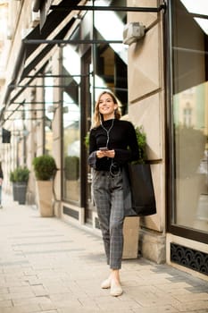 Young woman on the street with mobile phone and listening music