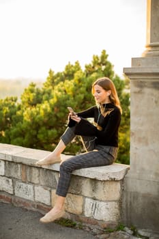 Portrait of young woman holding mobile phone while sitting on the wall